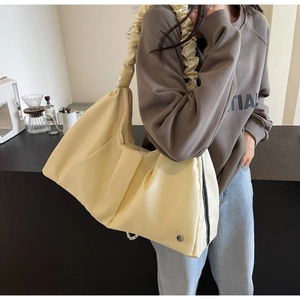 Dettaglio di una grande borsa a tracolla a pieghe color crema con tracolla in pizzo arricciato