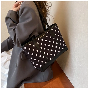 Detailed view of polka dot tote bag with gold logo on a model in a grey blazer