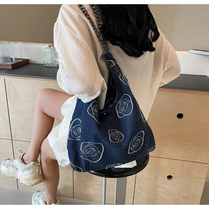 Detail view of denim shoulder bag featuring artistic white rose patterns and metal chain strap