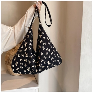 Detail of black canvas shoulder bag featuring dense cream-colored bow pattern with wide strap
