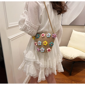 Detail of sweet woven straw crossbody bag with colorful 3D floral accents on white dress