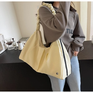 Ampia borsa a spalla plissettata beige da donna mostrata in un ambiente cafe trendy