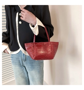 Detail of red crocodile embossed leather tote bag with metallic feet and structured handles