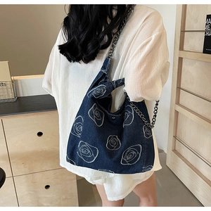 Detail of blue denim shoulder bag with white rose pattern and silver metal chain strap