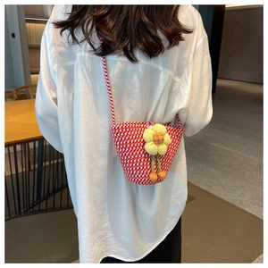 Detail of red and white woven crossbody bag with yellow sunflower plush charm on a model