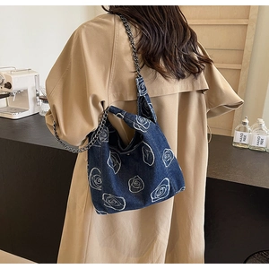 Detail shot of navy denim tote bag featuring white rose embroidery and metal chain strap