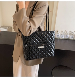 Detail of a large black quilted PU leather tote bag with silver logo on a brown blazer