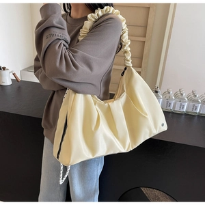 Dettaglio della borsa a nuvola color crema in raso con tracolla a balze e finitura lucida