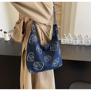 Detail shot of navy denim shoulder bag featuring white rose floral embroidery and metal chain