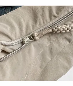 Detalle de cerca de la cremallera de metal liso y el tirador trenzado en un bolso beige