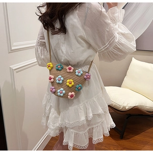 Close-up of handmade straw crossbody bag featuring colorful 3D plush flowers and brown strap