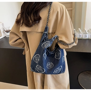 Detail of blue denim shoulder bag with white rose embroidery and vintage metal chain strap