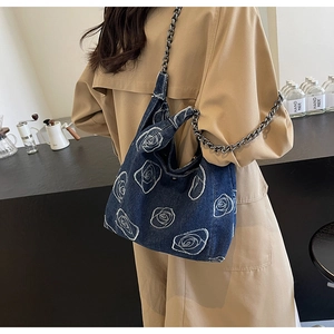 Detail of blue denim bag with white rose embroidery and silver metal chain strap