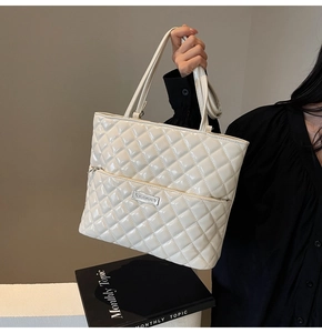 Detail of quilted cream tote bag with glossy finish and metal logo plaque on front