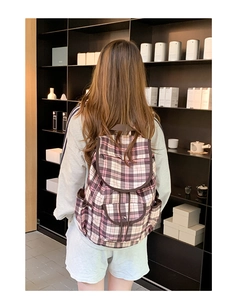 Rear view of model wearing pink plaid nylon backpack with flap closure and side pockets