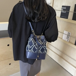 Fashionable denim bucket bag with white diamond fringe pattern and leather patchwork detail
