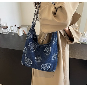 Detail of dark blue denim tote with white rose embroidery and metal chain strap on model