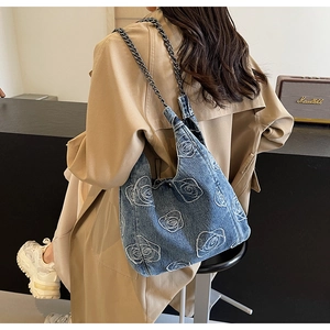 Detail of blue denim shoulder bag with white rose embroidery and stylish metal chain