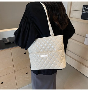 Close-up of a white quilted patent leather tote bag with silver metal plaque logo