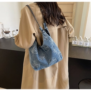 Detail of rose floral embroidery on blue denim shoulder bag with black metal chain strap