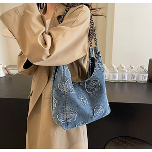 Detail of denim tote bag featuring white rose embroidery and dark metal chain strap