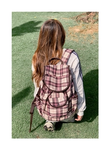 Detailed back view of a plaid nylon backpack worn by a model on green grass outdoors