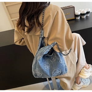 Detail of blue denim shoulder bag with white rose embroidery and metal chain strap