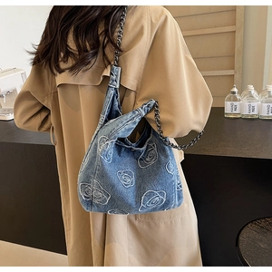 Detail of light blue denim hobo bag featuring white rose embroidery and metal chain strap
