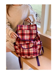 Detail view of the red and white tartan backpack showing canvas texture and purple straps