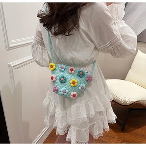 Close-up of a light blue woven crossbody bag with colorful 3D floral accents on a model