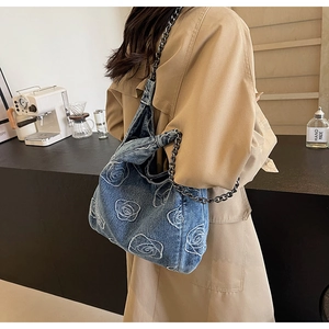 Detail of blue denim shoulder bag featuring white rose embroidery and thick metal chain strap