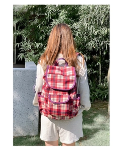 Detail of red and beige plaid nylon backpack with purple trim shown in an outdoor setting