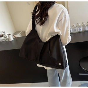 Dettaglio della borsa tote in nylon nero con tracolla a pieghe e logo bianco in un caffè