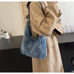 Close-up of blue denim tote bag featuring white rose embroidery and metal chain strap