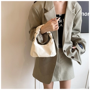 Detail of a white croissant bag with gathered handle and polished leather finish