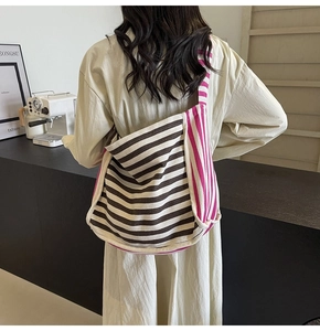 Rear view of a spacious striped canvas hobo tote bag worn by a model in a minimal setting