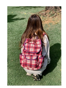 Outdoor view of a red and white checkered nylon backpack with front zipper pocket and flap