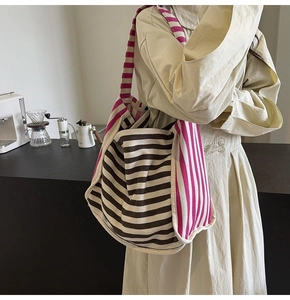 Detail view of large striped canvas tote bag with wide shoulder strap worn by a model