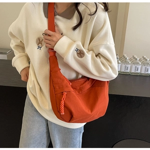 Detail of orange nylon dumpling bag showing thick woven zipper pull and crossbody strap
