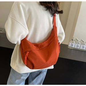 Detail of an orange nylon crescent crossbody bag featuring a woven zipper pull on model