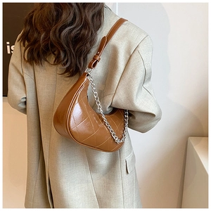 Détail du sac croissant matelassé marron caramel avec chaîne argentée sur un blazer