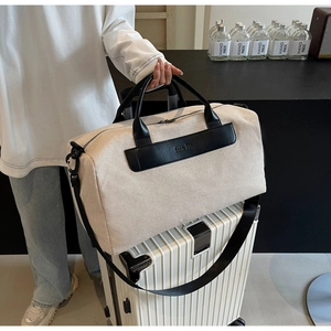 Detail of beige canvas travel bag with black leather accents and luggage sleeve