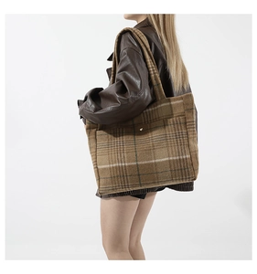 Détail d'un cabas en laine à carreaux marron avec boucle en métal sur un mannequin en cuir