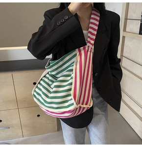 Detail of a large canvas hobo bag with green, pink, and white stripes on a female model