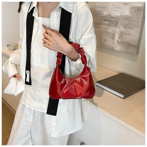 Detail of red crescent bag featuring glossy texture and ruched cloud handle