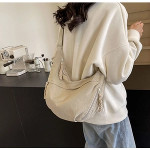 Detailed view of beige nylon crescent bag with woven zipper pull on a casual shoulder strap