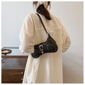 Detail of black glossy PU shoulder bag featuring silver studs and western buckle on model