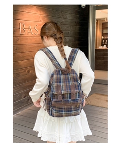 Detail of vintage plaid wool backpack with brown leather straps and metal eyelet accents