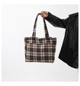 Détail de la texture en laine à carreaux marron et du bouton pression doré du sac