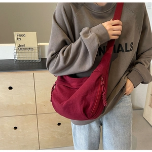 Close-up of a dark red nylon crescent crossbody bag worn by a model in a casual setting